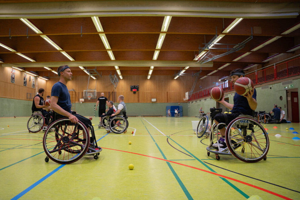 Wheelchair basketball players practicing in a gymnasium, captured by content creators for a documentary. The scene offers excellent stock footage for video editors.